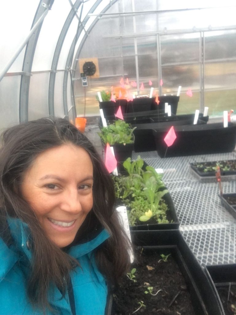Tanya smiling with her microgreens in her greenhouse during the winter.