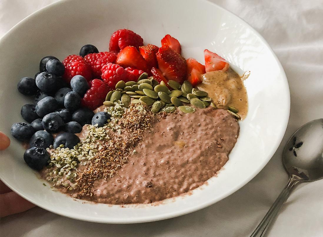 Chocolate Coconut Chia Pudding in a white bowl with fresh berries, pumpkin seeds and almond butter