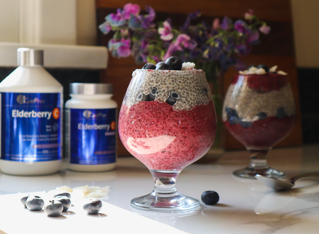 vibrant elderberry burst vanilla and berry layered chia pudding parfait in a glass garnished with blueberries