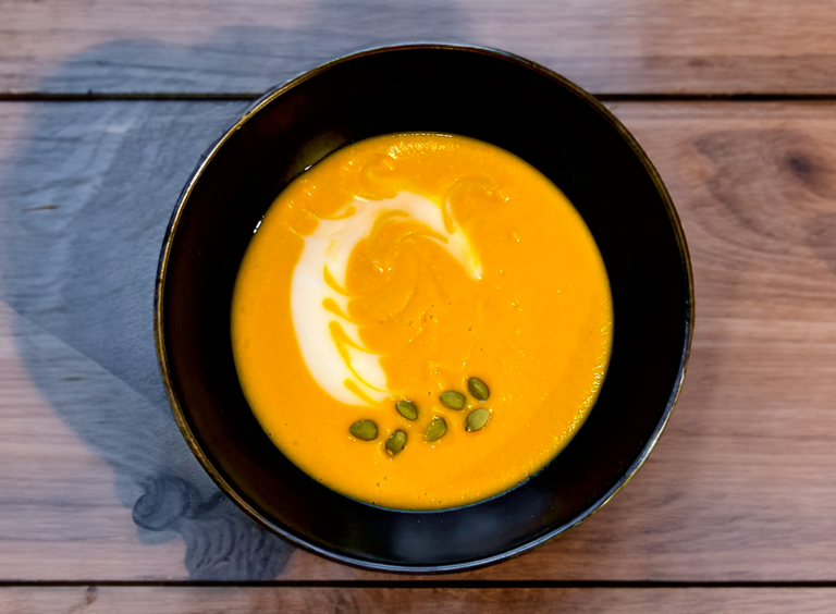 Curried Collagen Butternut Squash Soup in a black soup bowl, topped with cream and pumpkin seeds