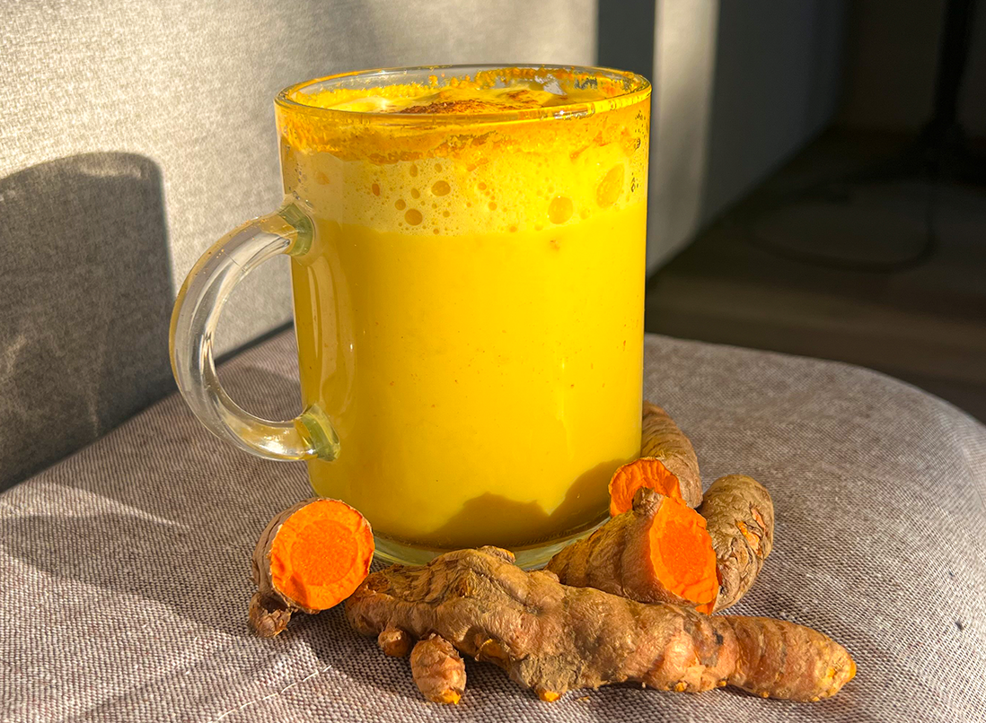 Golden and frothy Anti-Inflammatory Turmeric Latte in a glass mug, surrounded by turmeric root