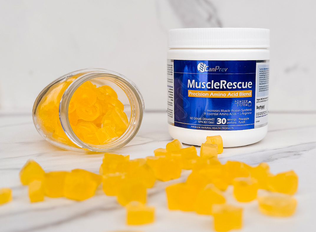 Yellow MuscleRescue Pineapple Gummies pouring out of a jar on the counter beside the MuscleRescue tub