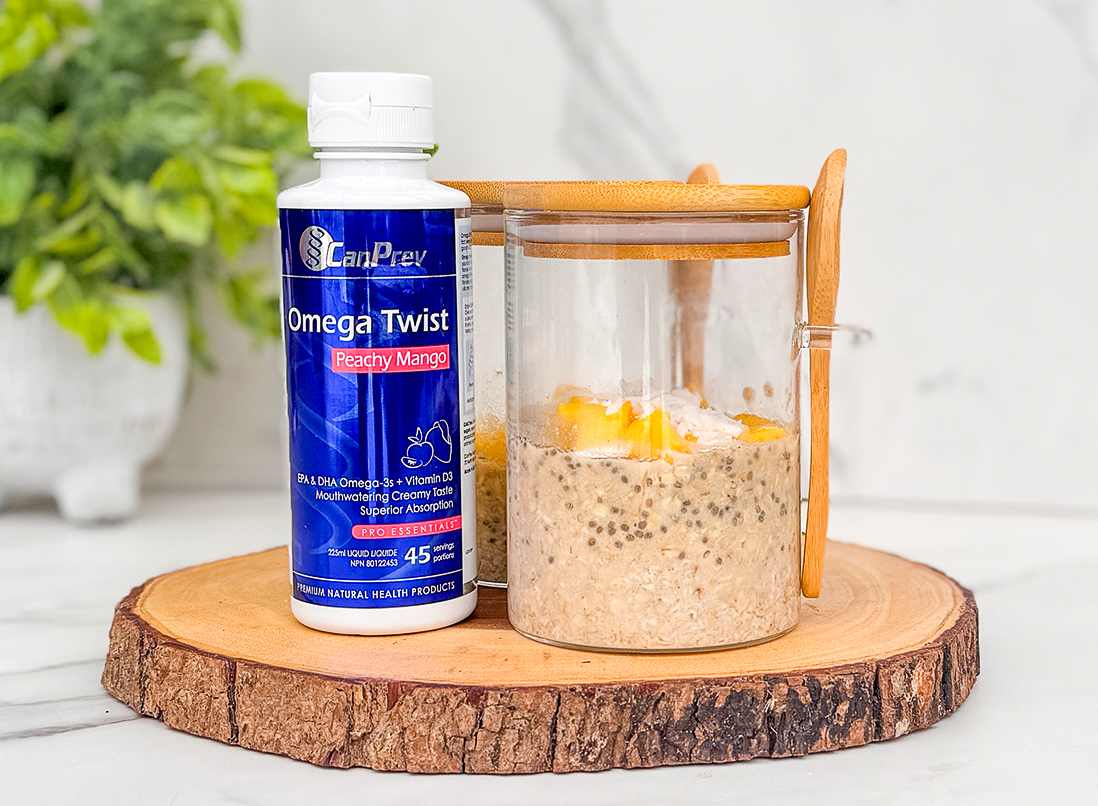 Peachy Mango Overnight Oats in a glass jar with a bamboo lid and spoon. The Omega Twist is standing beside it on the kitchen counter.