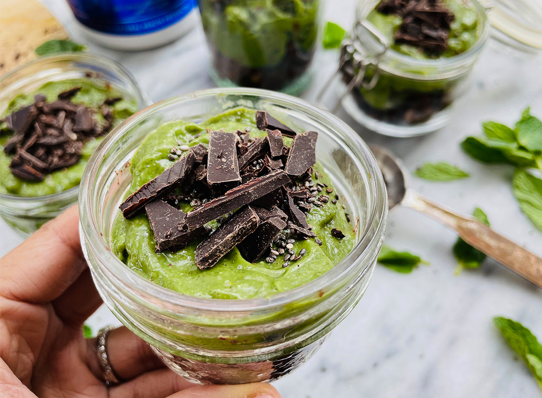 vibrant green happy go lucky mint chia pudding in a glass jar garnished with dark chocolate.
