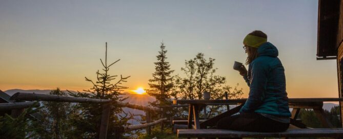 Woman having coffee outdoors early in the morning, looking at the sunrise.