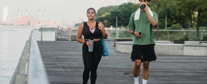 Woman and man in workout clothing walking along a board walk with water bottles in their hands