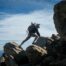 Man climbing rocks outdoors, with blue skies above him and a backpack on his back.