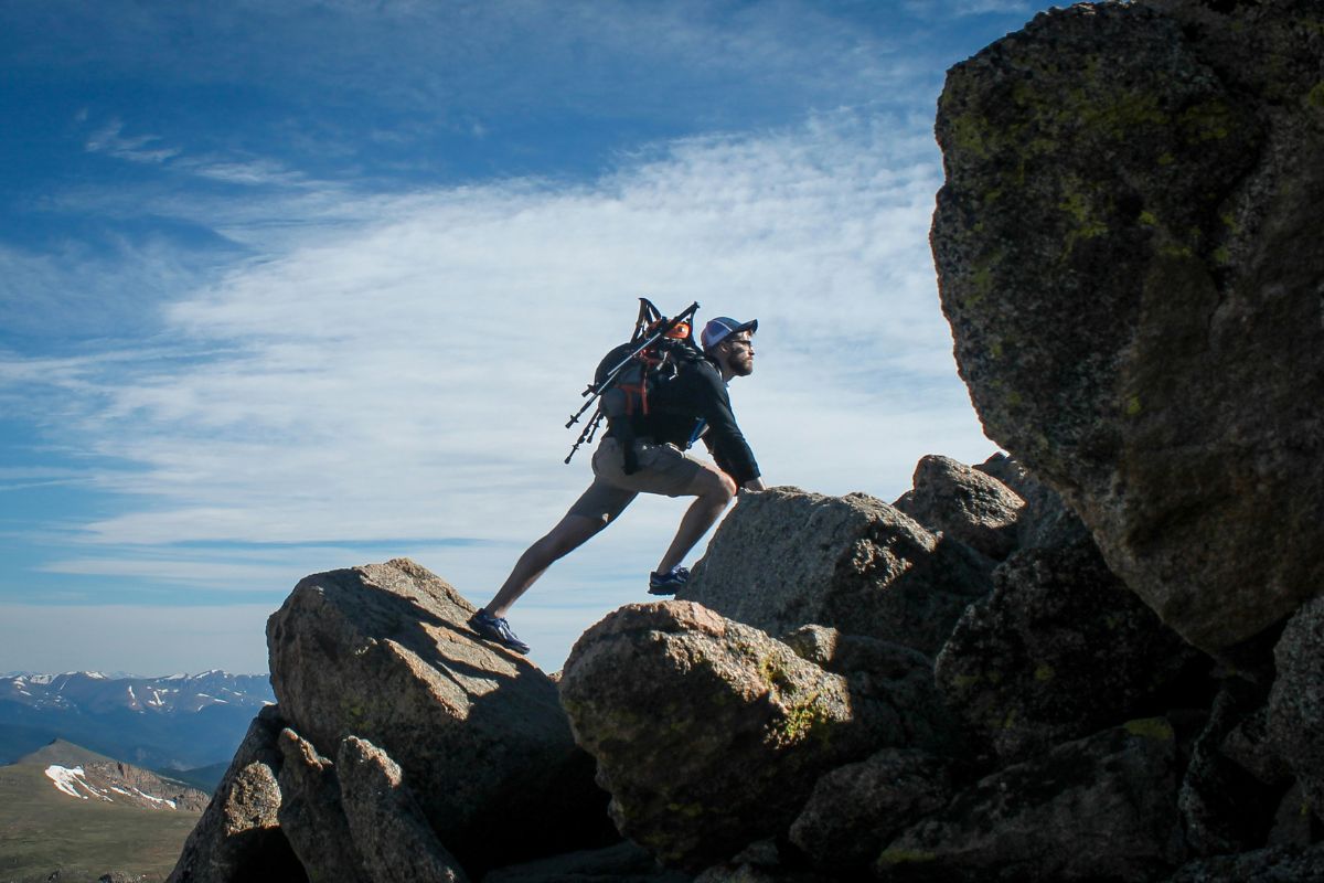 Man climbing rocks outdoors, with blue skies above him and a backpack on his back.