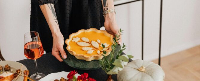 Fall food table display with woman's hand holding a pumpkin pie