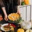 Fall food table display with woman's hand holding a pumpkin pie