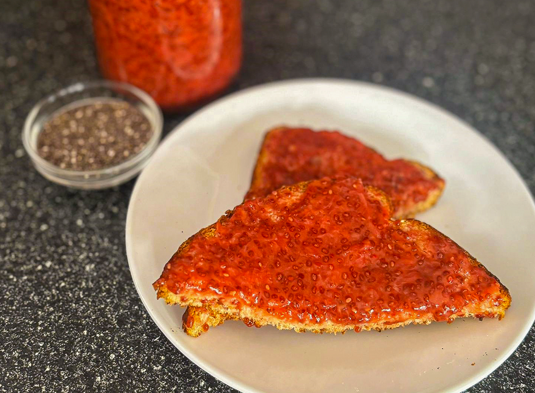 BP&J toast on a white plate with red strawberry chia seed jam. Strawberry jam and chia seeds in the background.