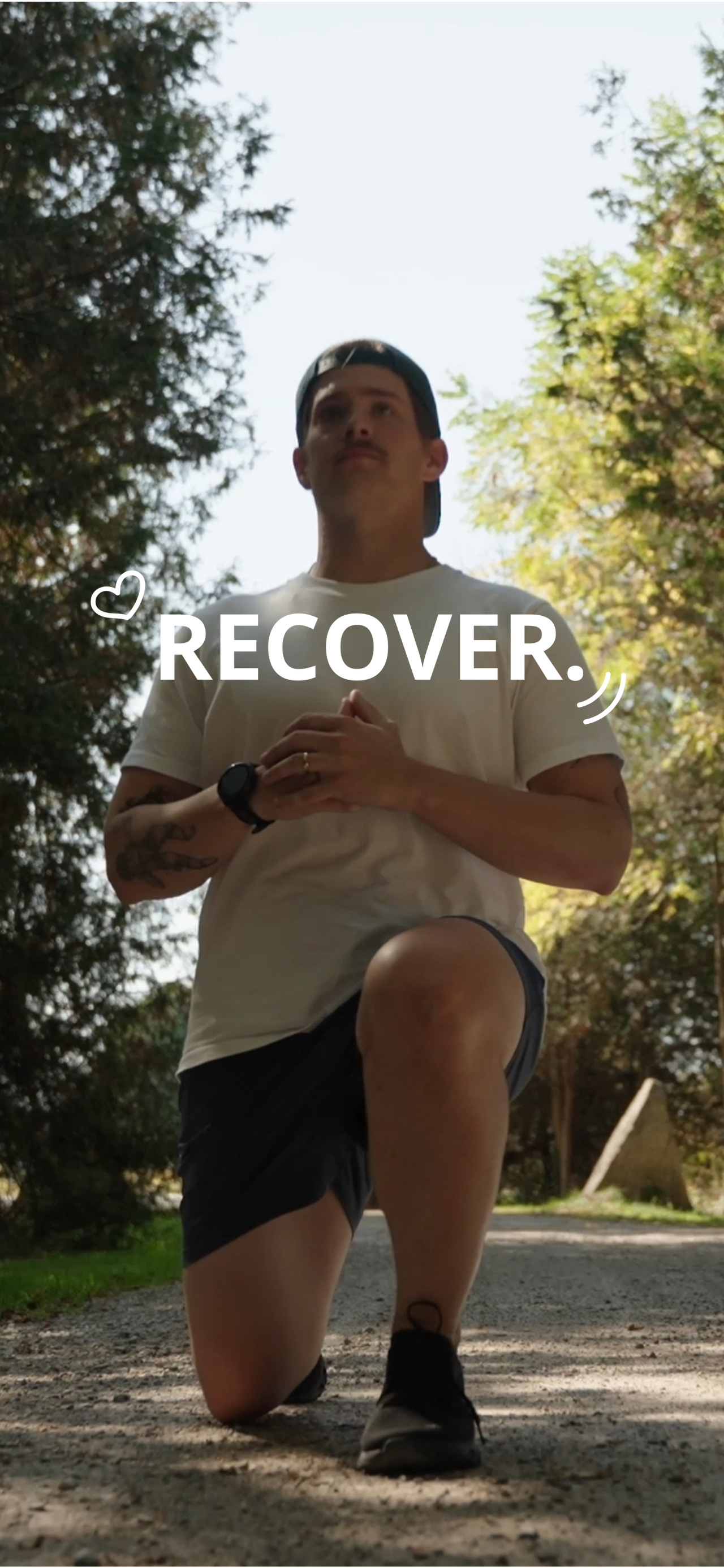 Man kneeling on a gravel path in a park, hands clasped, wearing a white T-shirt, shorts, and a backward cap, with 'RECOVER' overlay.