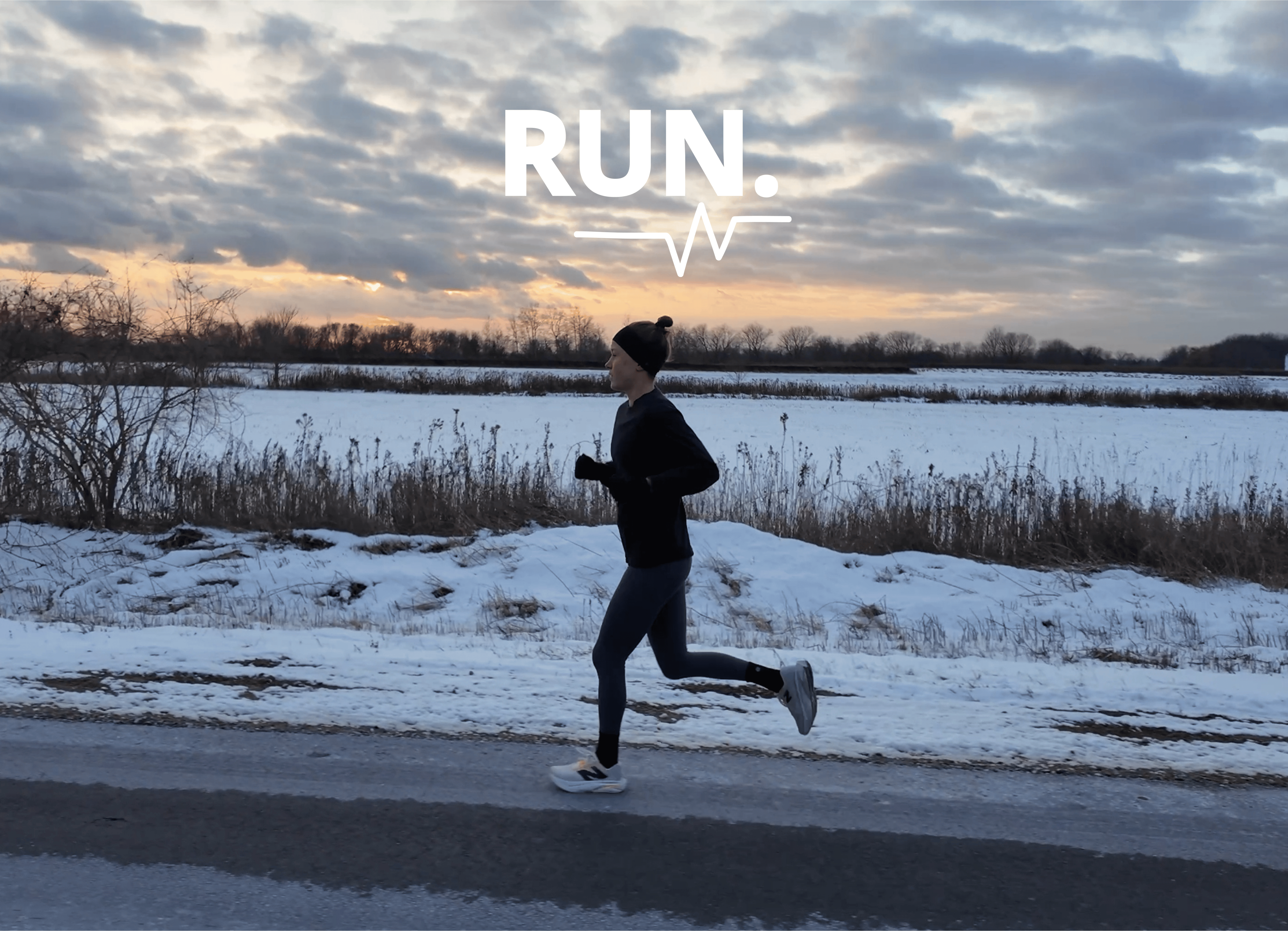 A person running along a snow-covered field beside a road at dusk, wearing a black beanie and black athletic gear.