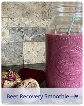 Beet recovery smoothie in a mason jar with a blue straw on a kitchen counter, with fresh beets beside it.