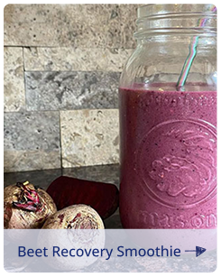 Beet recovery smoothie in a mason jar with a striped straw, next to whole beets on a kitchen counter.