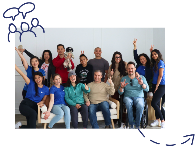 Group of diverse people posing for a photo indoors, with a small dog held up front center and several making peace signs.