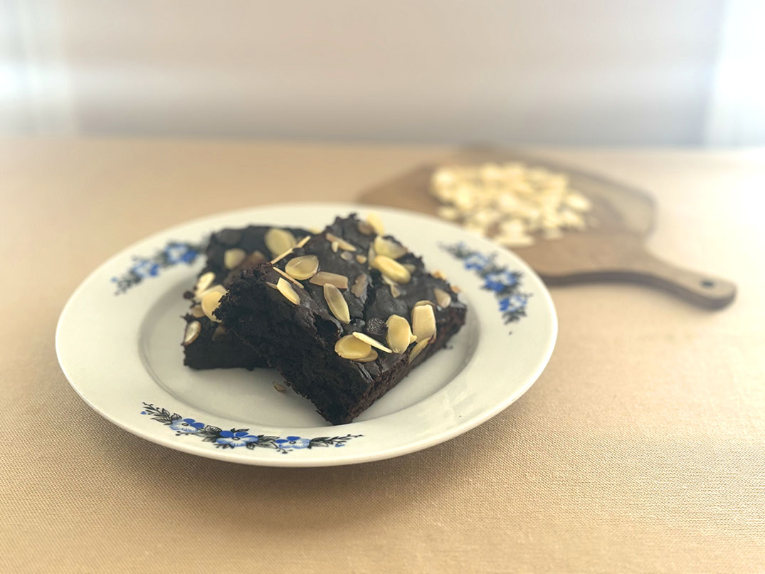 Two square chocolate brownies topped with almond slices on a white plate with blue floral rim.