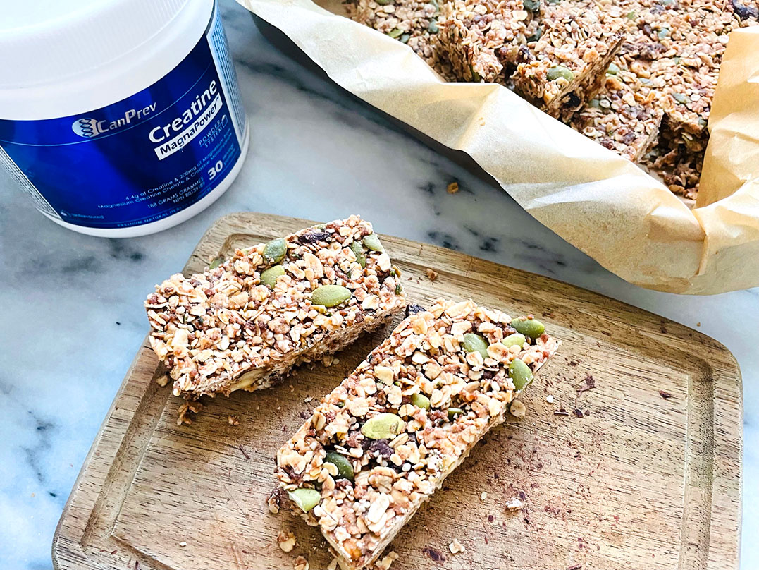 Two oat granola bars studded with pumpkin seeds and nuts on a wooden board with a CanPrev Creatine container in the background,