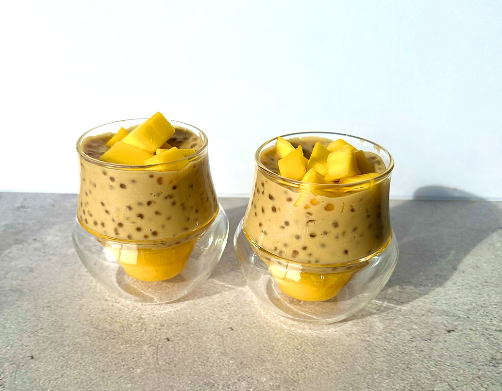 Two double‑walled glass cups of mango sago pudding with tapioca pearls, topped with mango chunks.